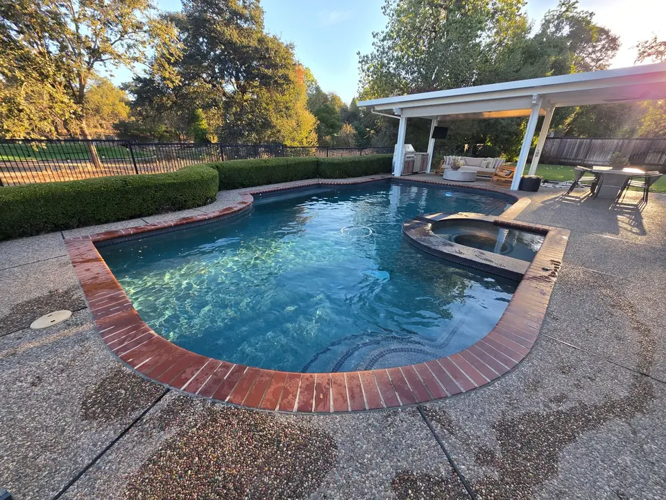 Sparkling blue water fills a brick-edged pool with an attached spa, curved steps, and landscaped surroundings, after pool service in Roseville, CA