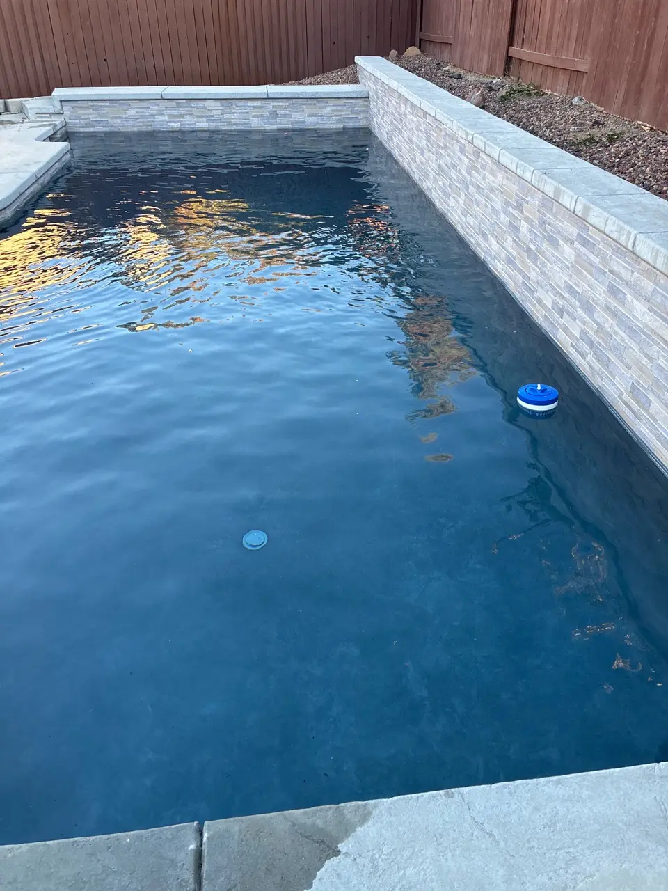 Clear blue pool water bordered by light stone coping and a raised tiled wall, after pool service in Roseville, CA