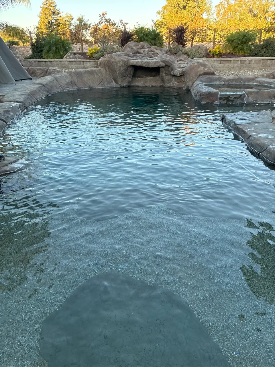 Clear blue pool water surrounds a pebble-finished entry, with rock edging, a grotto, and a raised spa, after pool service in Roseville, CA