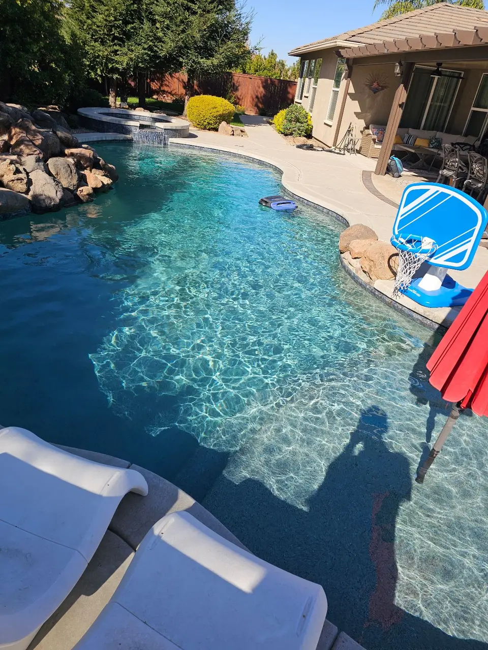 Sparkling turquoise pool with a raised spillover spa, rock work, shallow sun shelf, and in-water loungers, after pool service in Roseville, CA