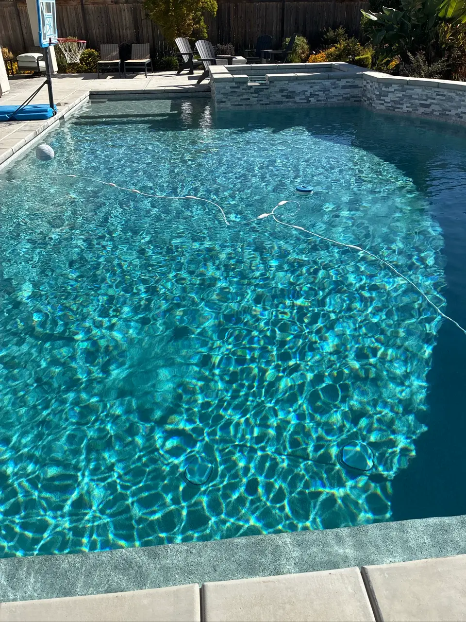 Sparkling blue pool water surrounds a shallow shelf beneath a raised tiled spa, with patio seating and landscaping, after pool service in Roseville, CA