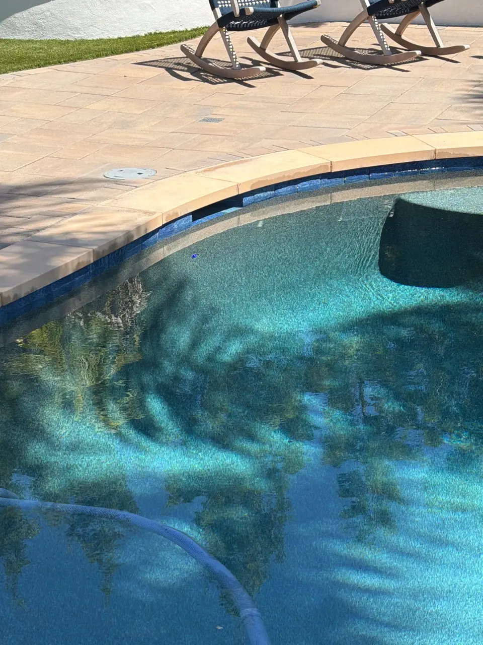 Clear turquoise pool water reveals a textured finish and submerged bench beneath blue tile and curved stone coping, after equipment install in San Diego, CA