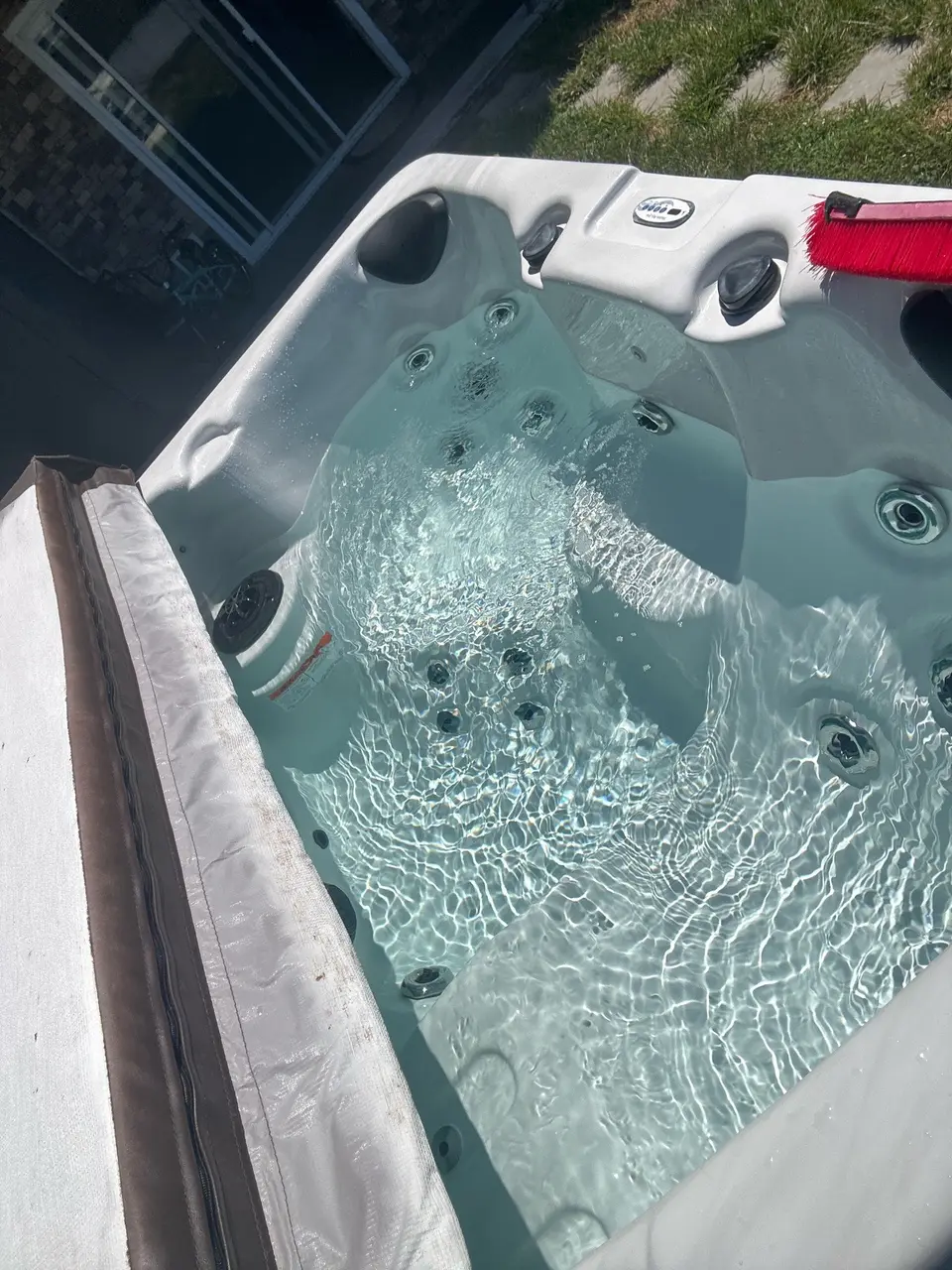 Clear, sparkling spa water reveals white molded seating and multiple jets, with a folded cover alongside, after pool service in San Diego, CA