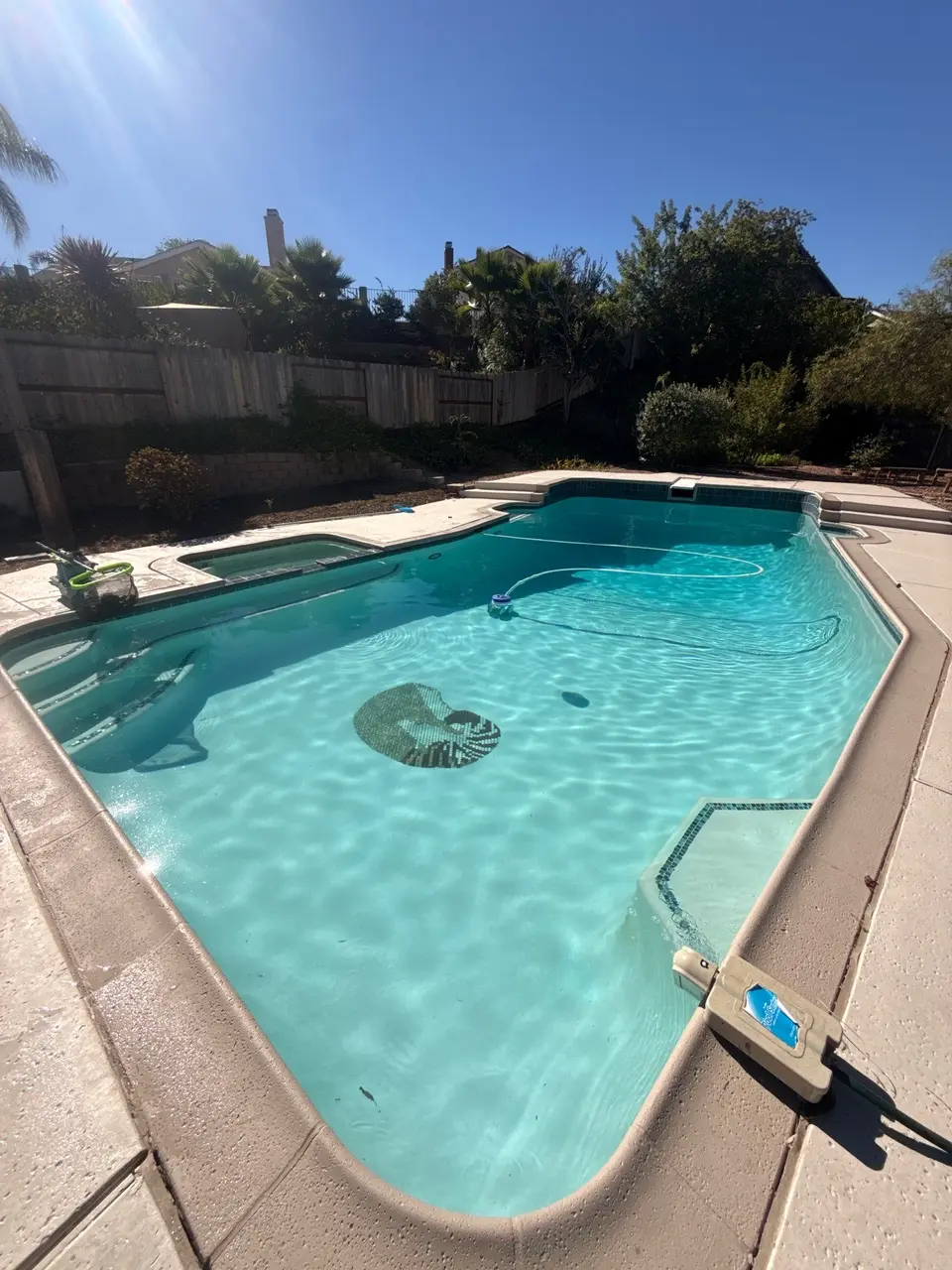 Sparkling turquoise pool with an attached spa, entry steps, underwater mosaic, and surrounding landscaping, after pool service in San Diego, CA