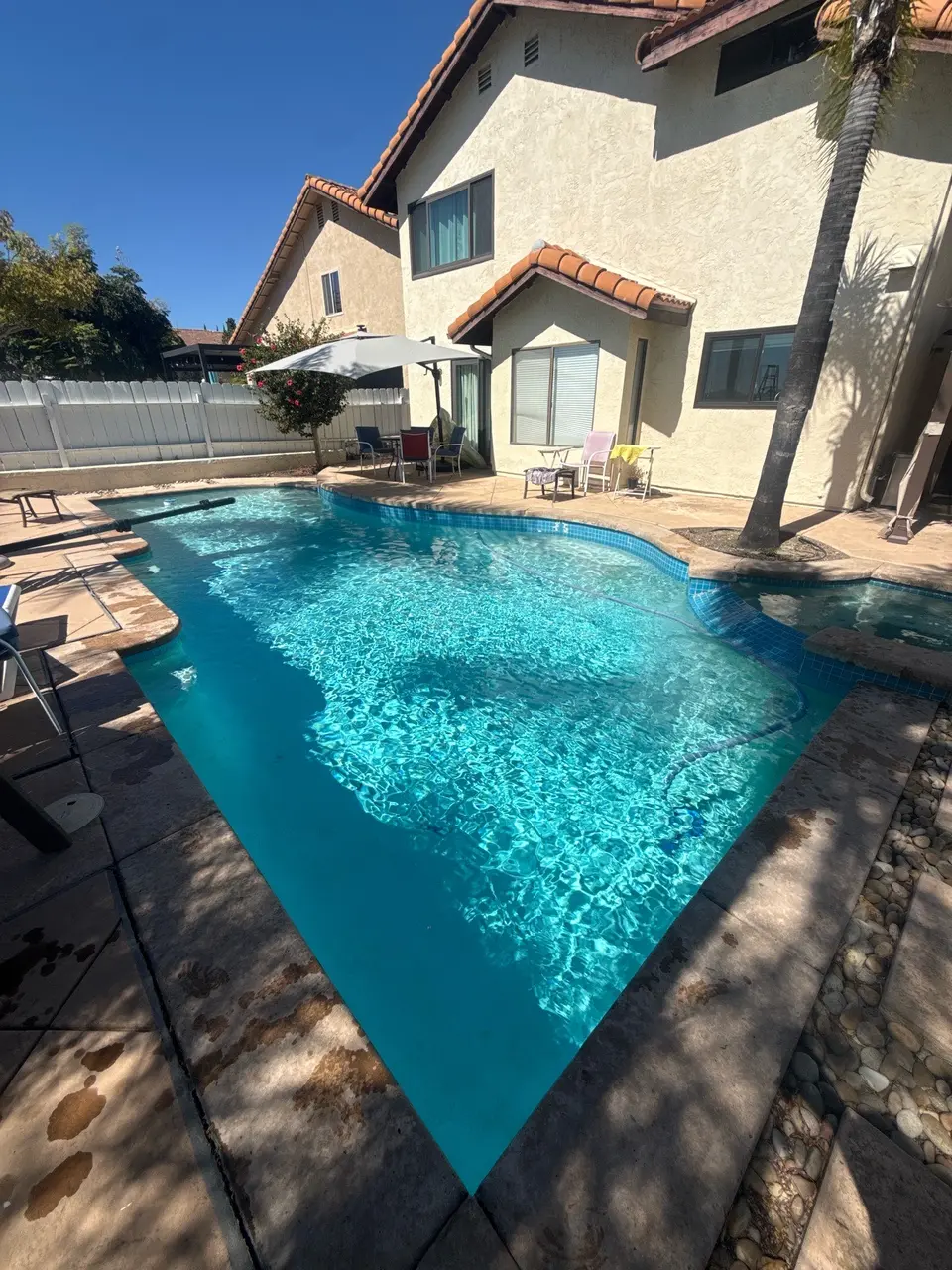 Pool and attached spa with sparkling turquoise water, blue tile, stone coping, and a palm-lined patio, after pool service in San Diego, CA