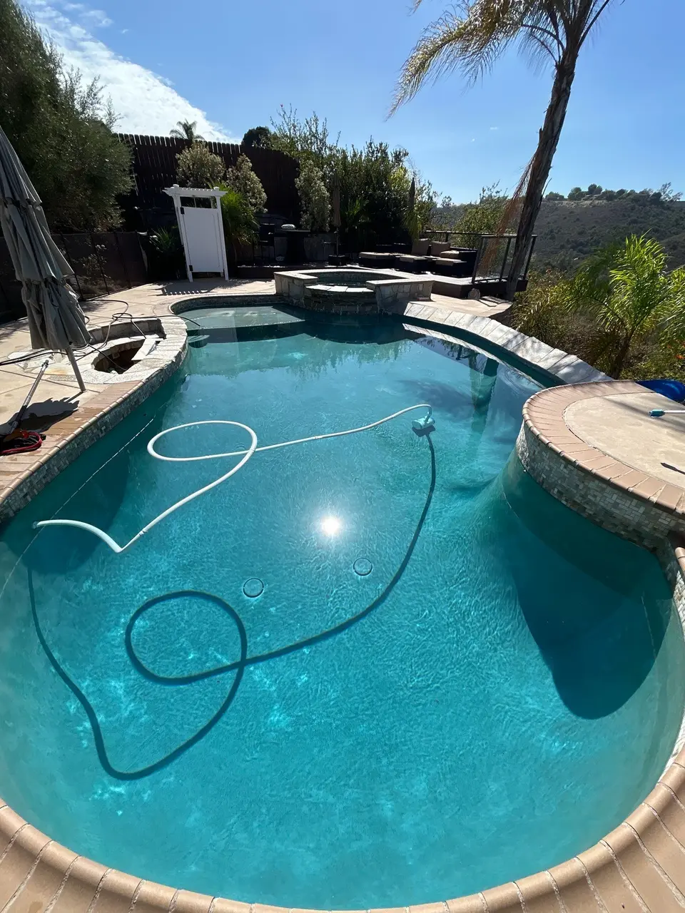 Sparkling turquoise water fills a freeform pool with a raised spa, tiled edges, and surrounding palms, after pool service in San Diego, CA