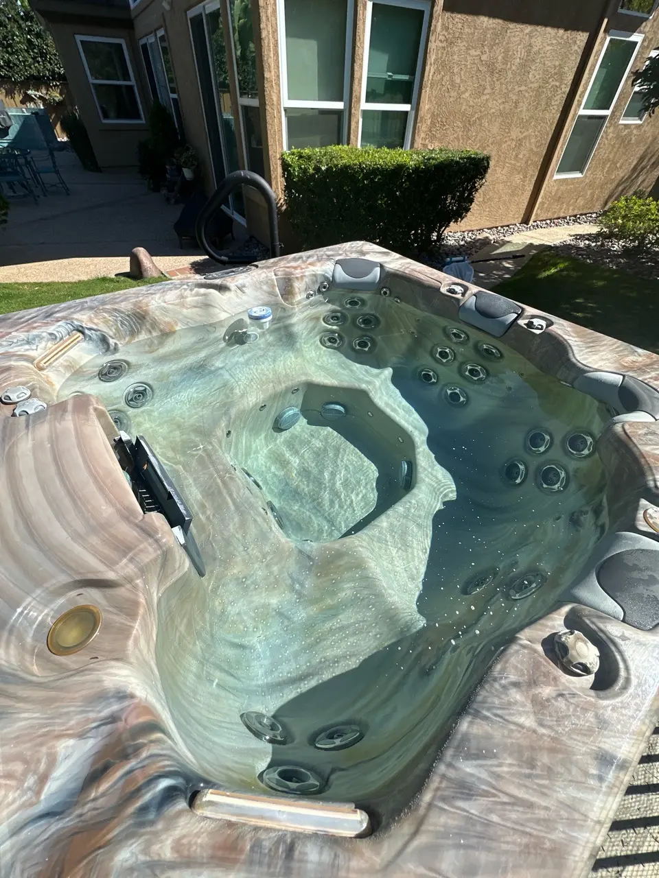 Clear water reveals a marbled spa shell with contoured seating, numerous jets, and padded headrests, after pool service in San Diego, CA