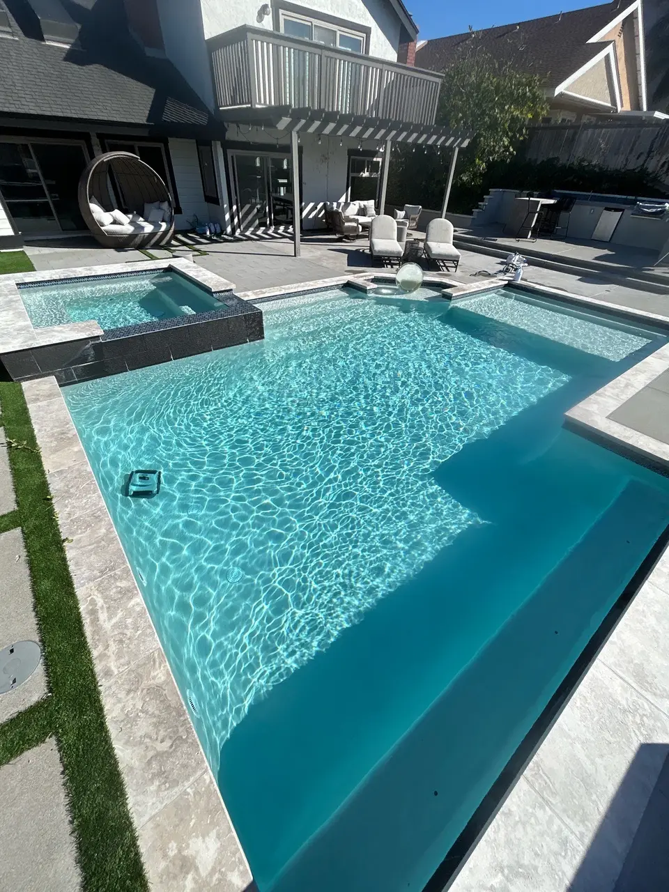 Sparkling turquoise pool with wide submerged steps, a raised tiled spa, and a furnished patio beneath a pergola, after pool service in San Diego, CA