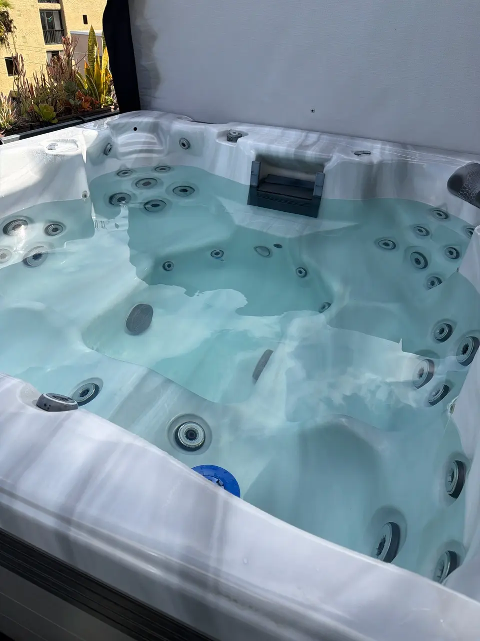 Clear pale blue water fills a white marbled spa with contoured seating and multiple massage jets, after pool service in San Diego, CA