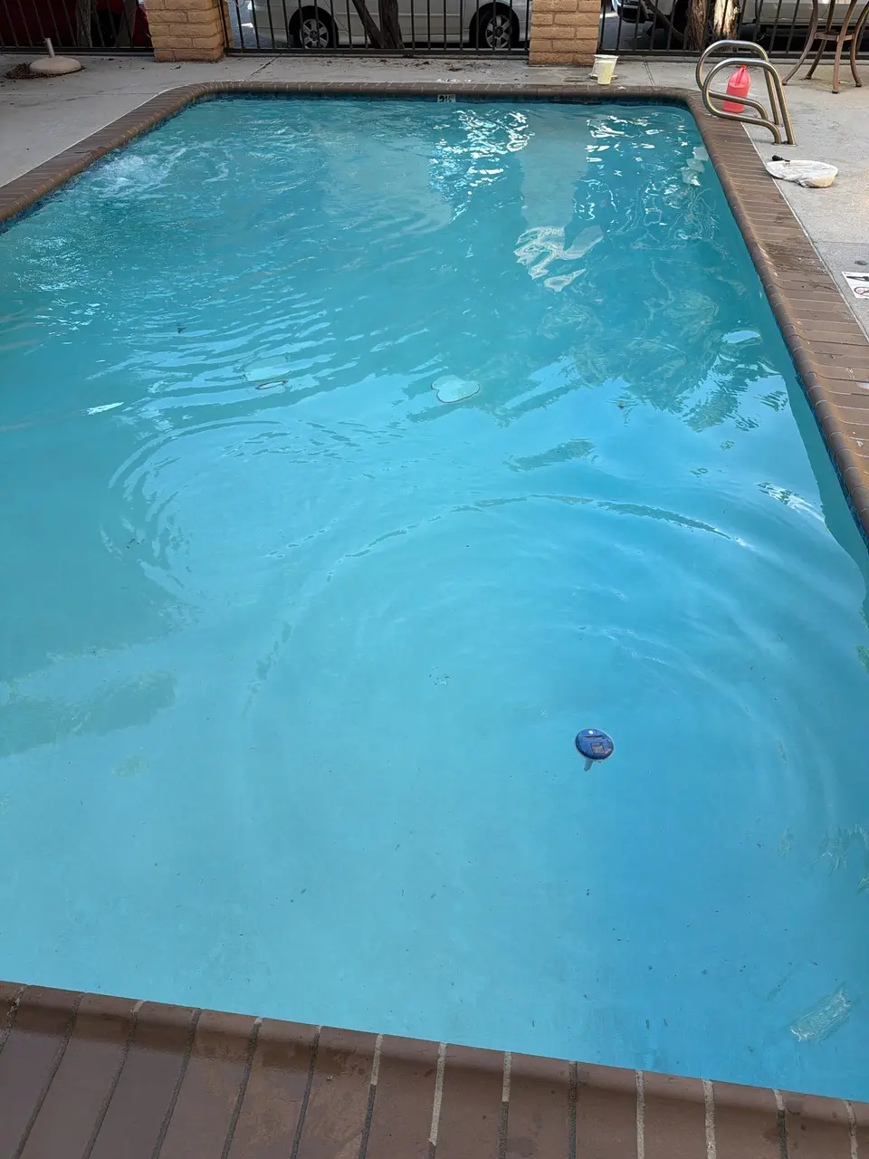 Rectangular pool with clear blue water, brick coping, a metal ladder, and visible floor discoloration, after pool service in San Diego, CA