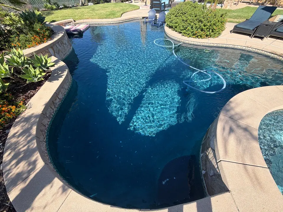 Sparkling blue water fills a freeform pool beside a raised spa, stone walls, and landscaped planters, after pool service in San Diego, CA