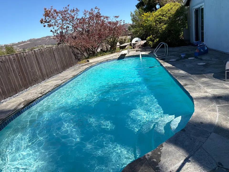 Sparkling turquoise pool water bordered by blue tile and stone decking, with a diving board and ladder, after equipment install in San Marcos, CA