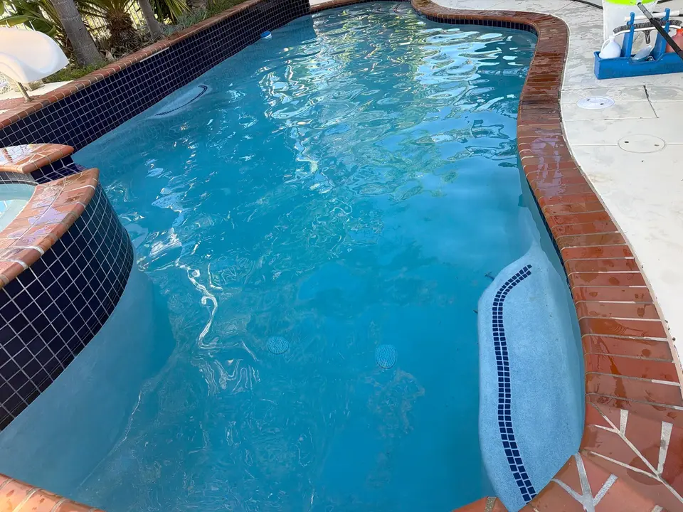 Clear blue pool water surrounds a raised tiled spa, with brick coping and a curved underwater bench, after pool service in San Marcos, CA