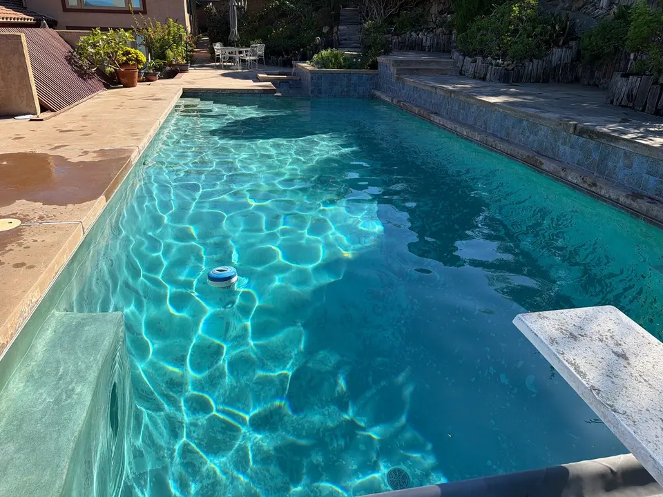 Sparkling turquoise pool with entry steps, a diving board, stone walls, and landscaped terraces, after pool service in San Marcos, CA