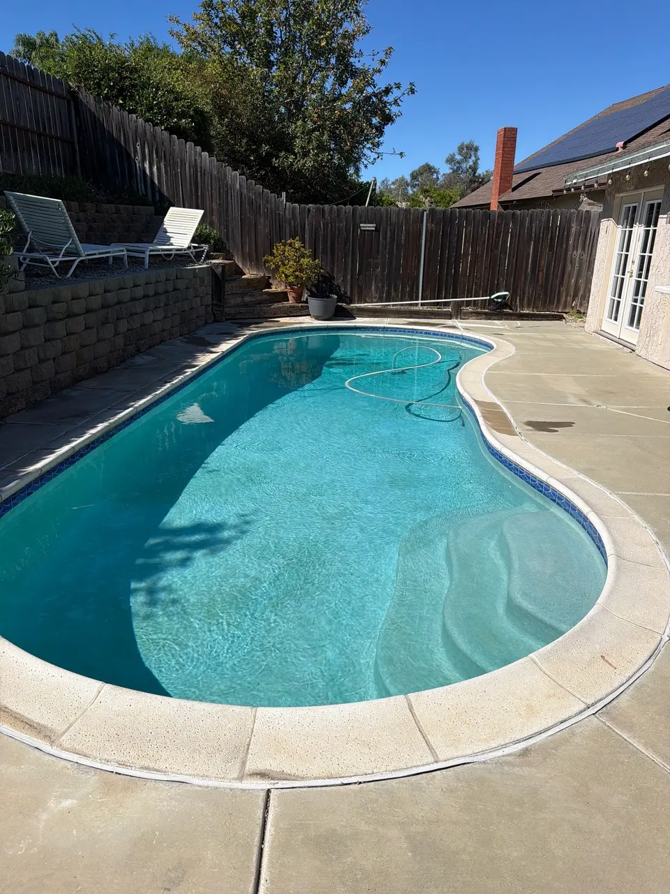 Sparkling turquoise water fills a curved pool with entry steps, blue tile, and a raised lounge area, after pool service in San Marcos, CA