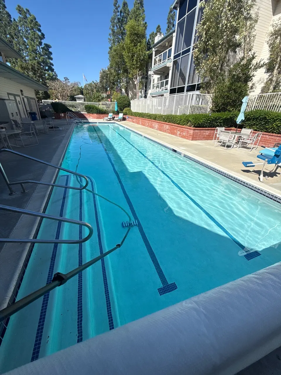 Sparkling blue water fills a rectangular lap pool with lane markings, entry steps, handrails, and poolside seating, after pool service in San Marcos, CA