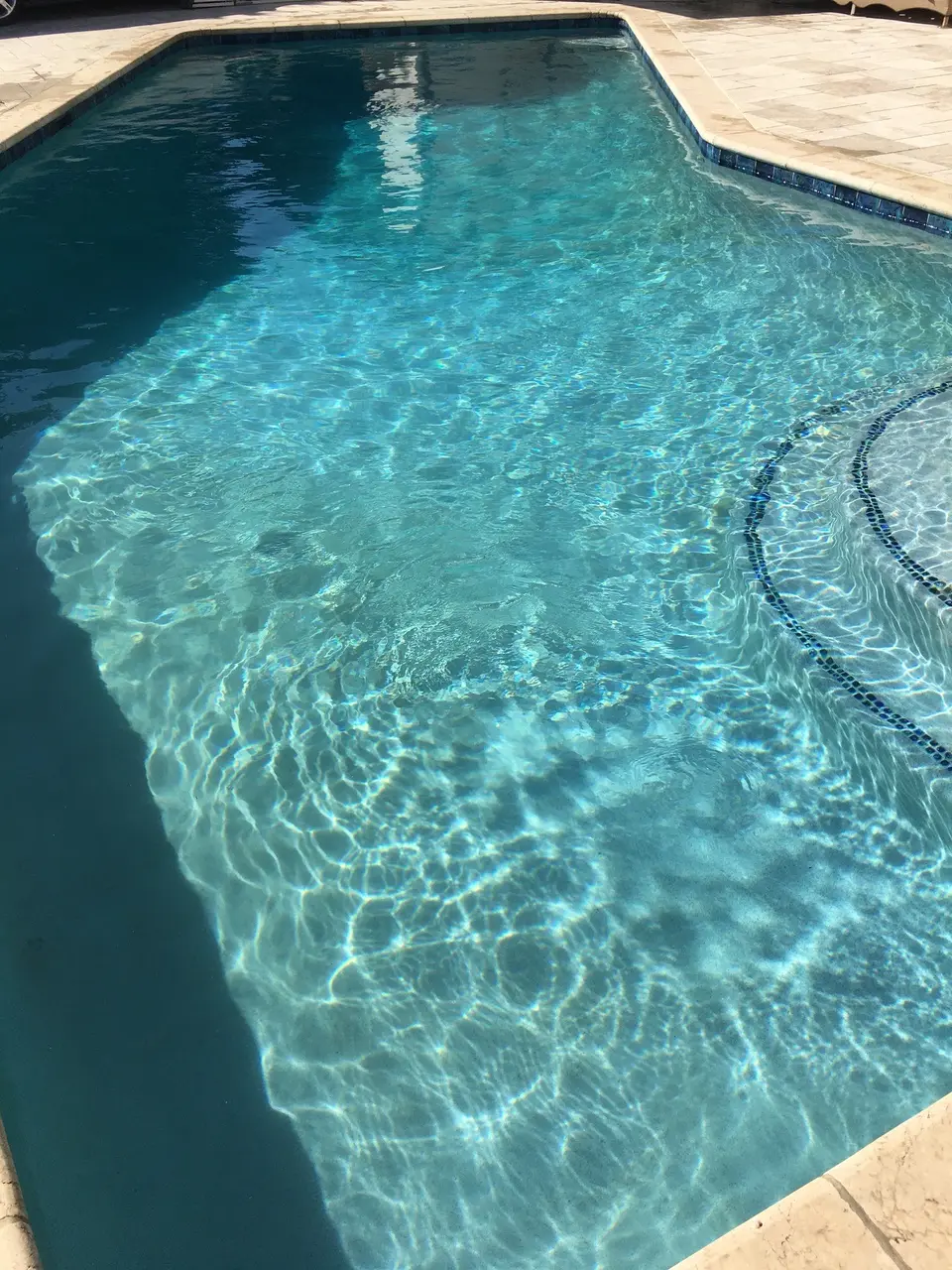 Sparkling turquoise pool water reveals a light finish and curved, blue-tile-edged steps beside a stone paver deck, after pool service in San Pedro, CA
