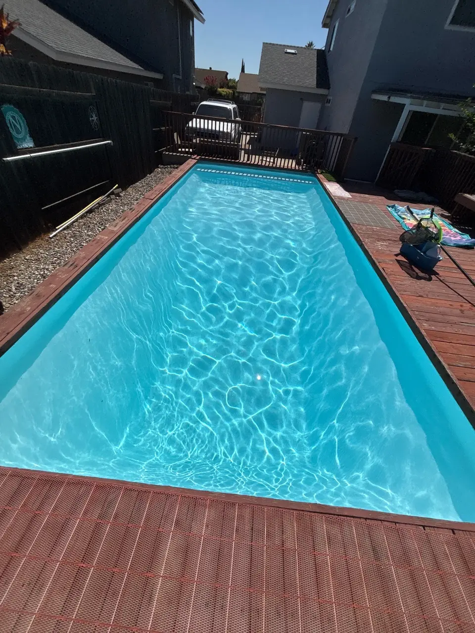 Rectangular pool with sparkling turquoise water, a light-colored finish, brick coping, and surrounding wood decking, after pool service in Santee, CA