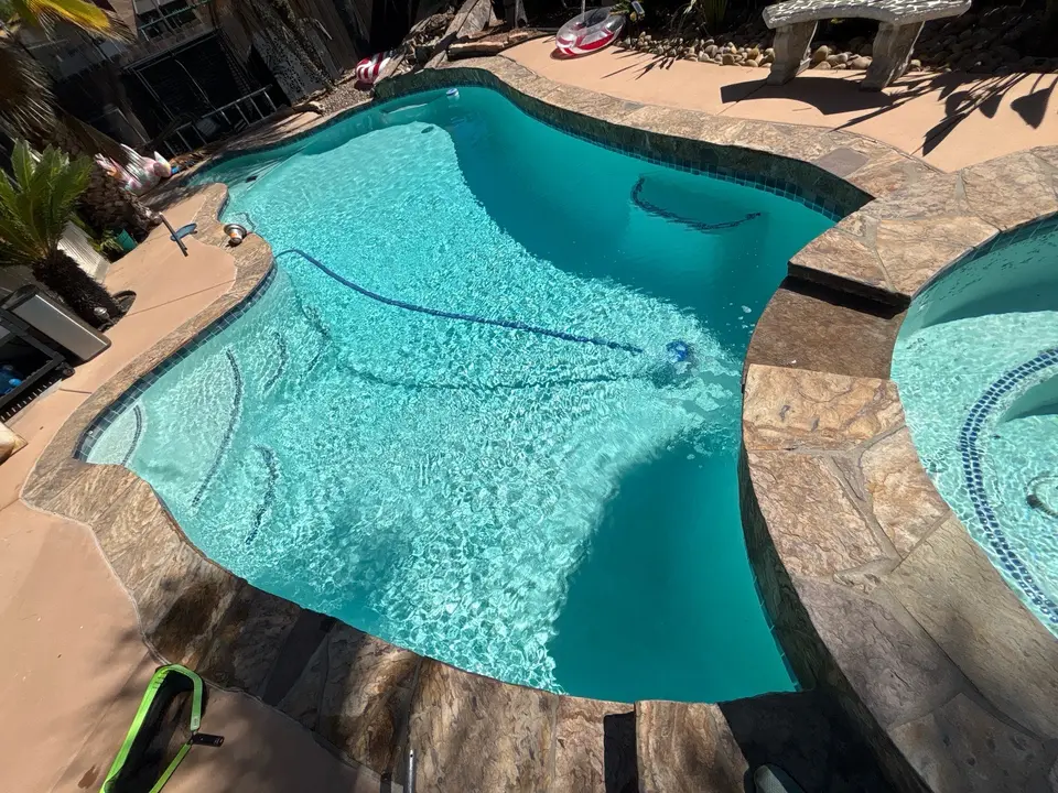 Sparkling turquoise water fills a freeform pool with decorative mosaics, stone coping, and an attached raised spa, after pool service in Santee, CA