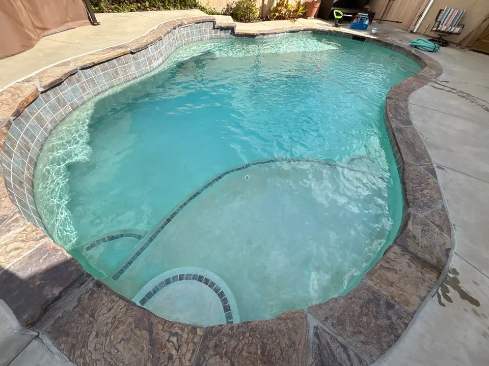 Clear turquoise water fills a freeform pool with stone coping, a raised tiled wall, and broad shallow entry, after pool service in Santee, CA