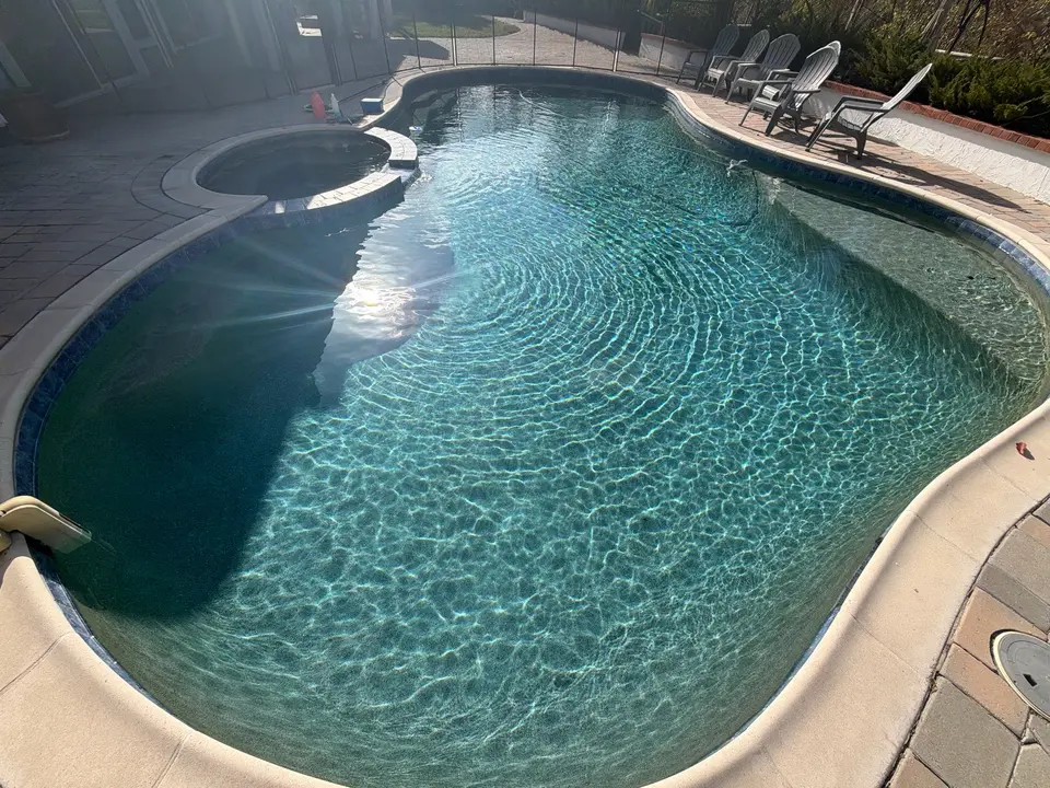 Sparkling turquoise water fills a freeform pool with an attached circular spa, blue tile, and submerged bench, after pool service in Scripps Ranch, CA
