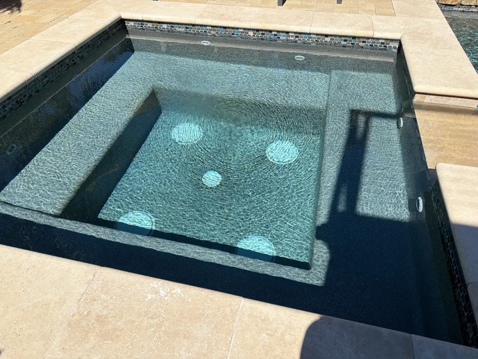 Spa with sparkling clear water, gray finish, built-in benches, mosaic waterline tile, and stone coping, after pool service in Solana Beach, CA