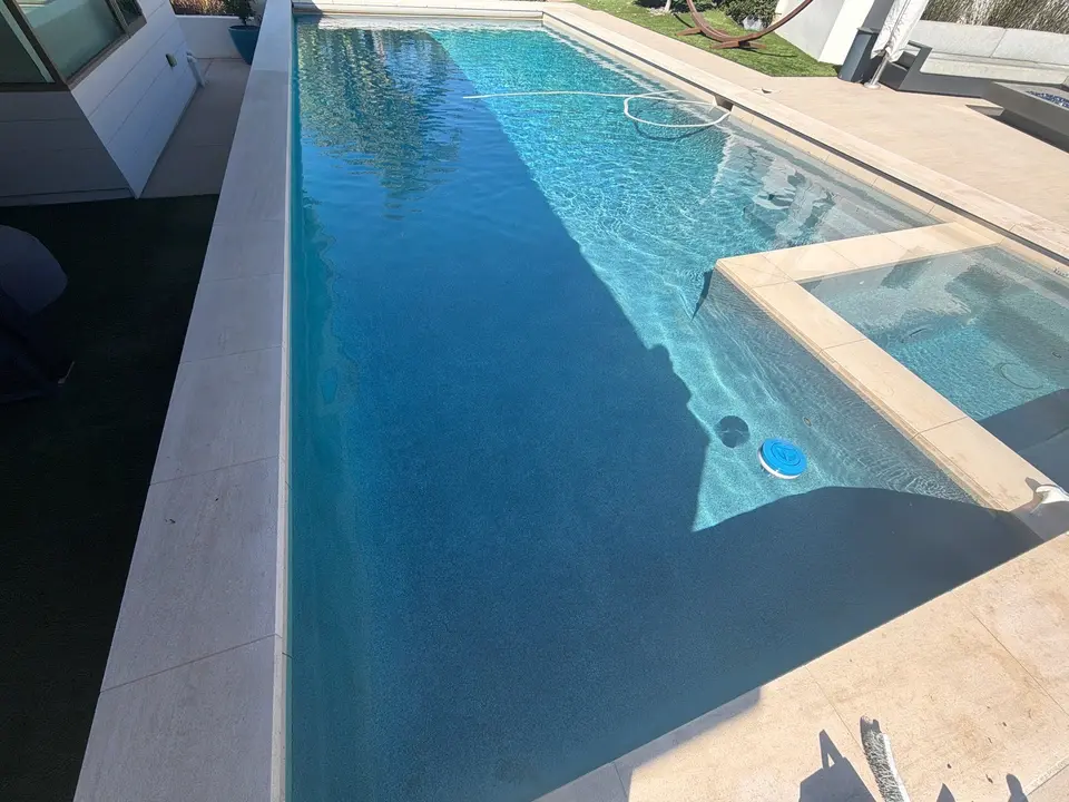 Clear blue water fills a rectangular pool with an attached spa, light stone coping, and nearby landscaping, after pool service in Solana Beach, CA