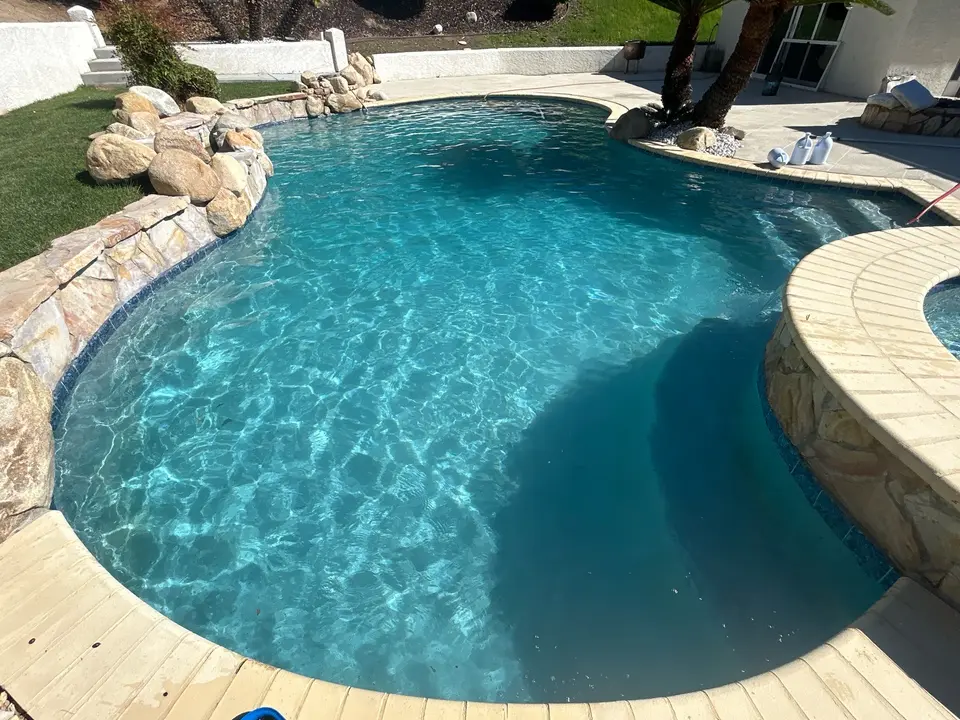 Sparkling turquoise water fills a freeform pool beside a raised spa, natural stone edging, and palm trees, after pool service in Temecula, CA