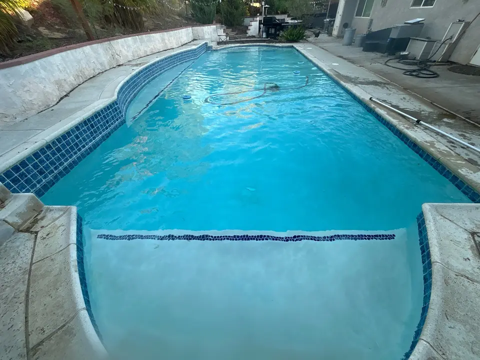 Clear blue water fills a long pool with broad entry steps, blue tile, and surrounding palms, after pool service in Temecula, CA