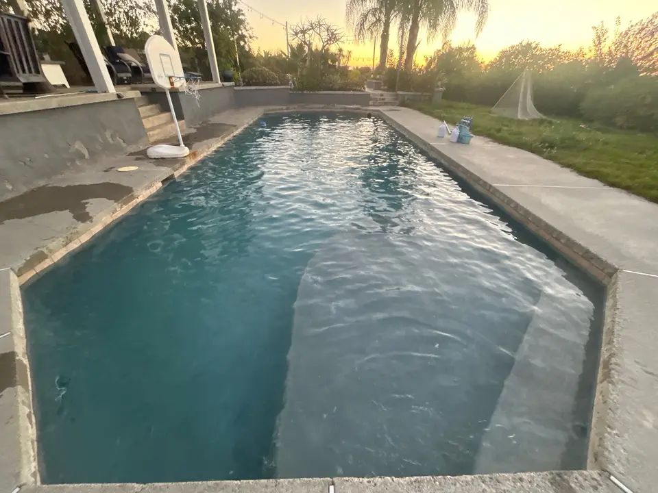 Clear blue water fills a long pool beside a basketball hoop, concrete deck, and palm-lined landscaping, after pool service in Temecula, CA