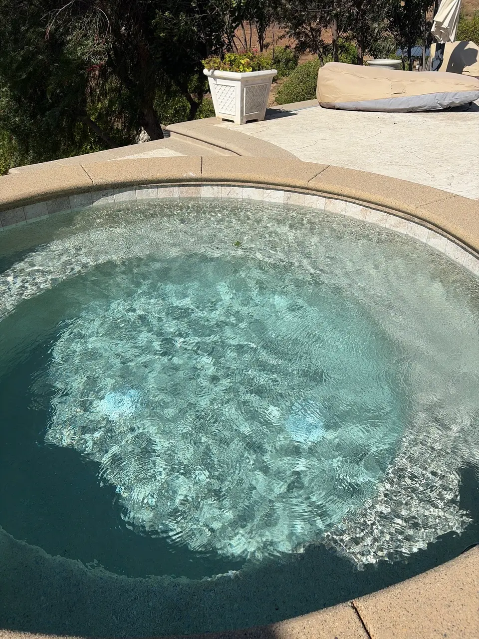 Rounded spa with sparkling turquoise water, submerged seating, waterline tile, and tan coping beside a landscaped patio, after pool service in Temecula, CA