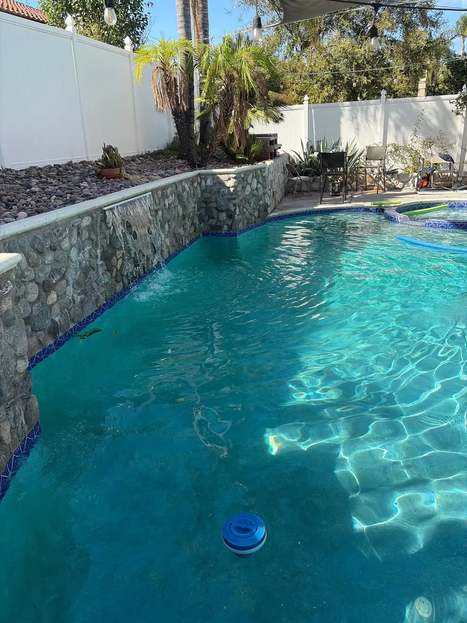 Clear turquoise pool water beside a stone waterfall wall, with a raised spa and palm landscaping, after pool service in Temecula, CA