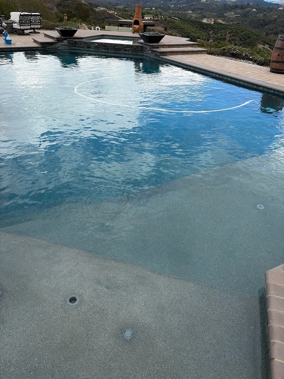 Clear blue pool with a broad shallow entry, raised tiled spa, and landscaped hillside views, after pool service in Temecula, CA