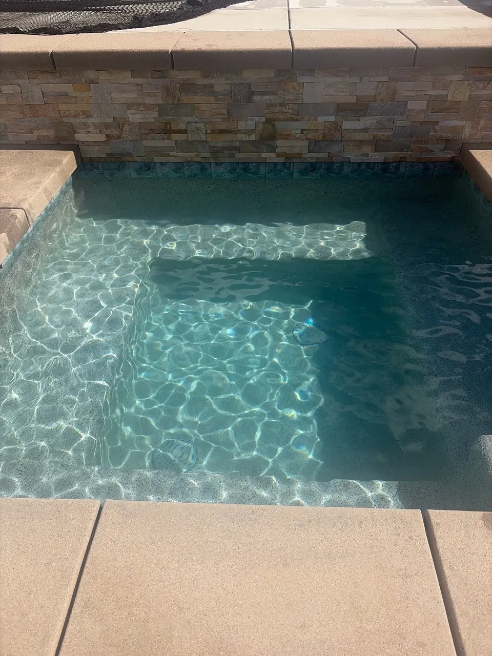 Clear turquoise spa water reveals a submerged bench and textured finish beneath a stacked-stone wall, after pool service in Temecula, CA