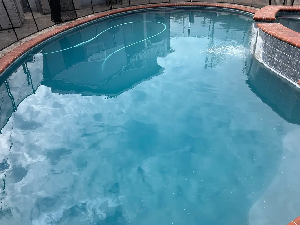 Clear blue pool water surrounds curved steps and a raised tiled spa with a spillover waterfall, after green 2 clean in Torrance, CA