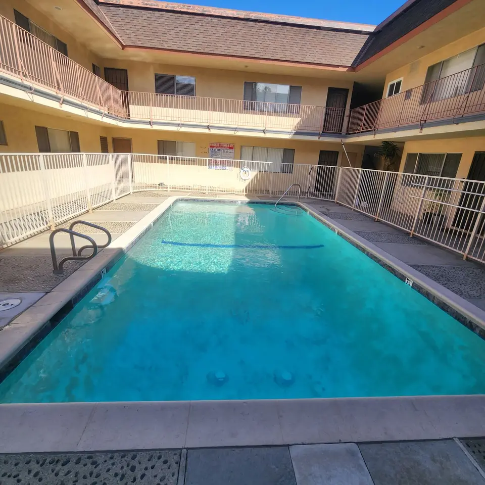 Clear turquoise water fills a rectangular courtyard pool with metal handrails, a blue floor stripe, and mottled finish, after pool service in Torrance, CA