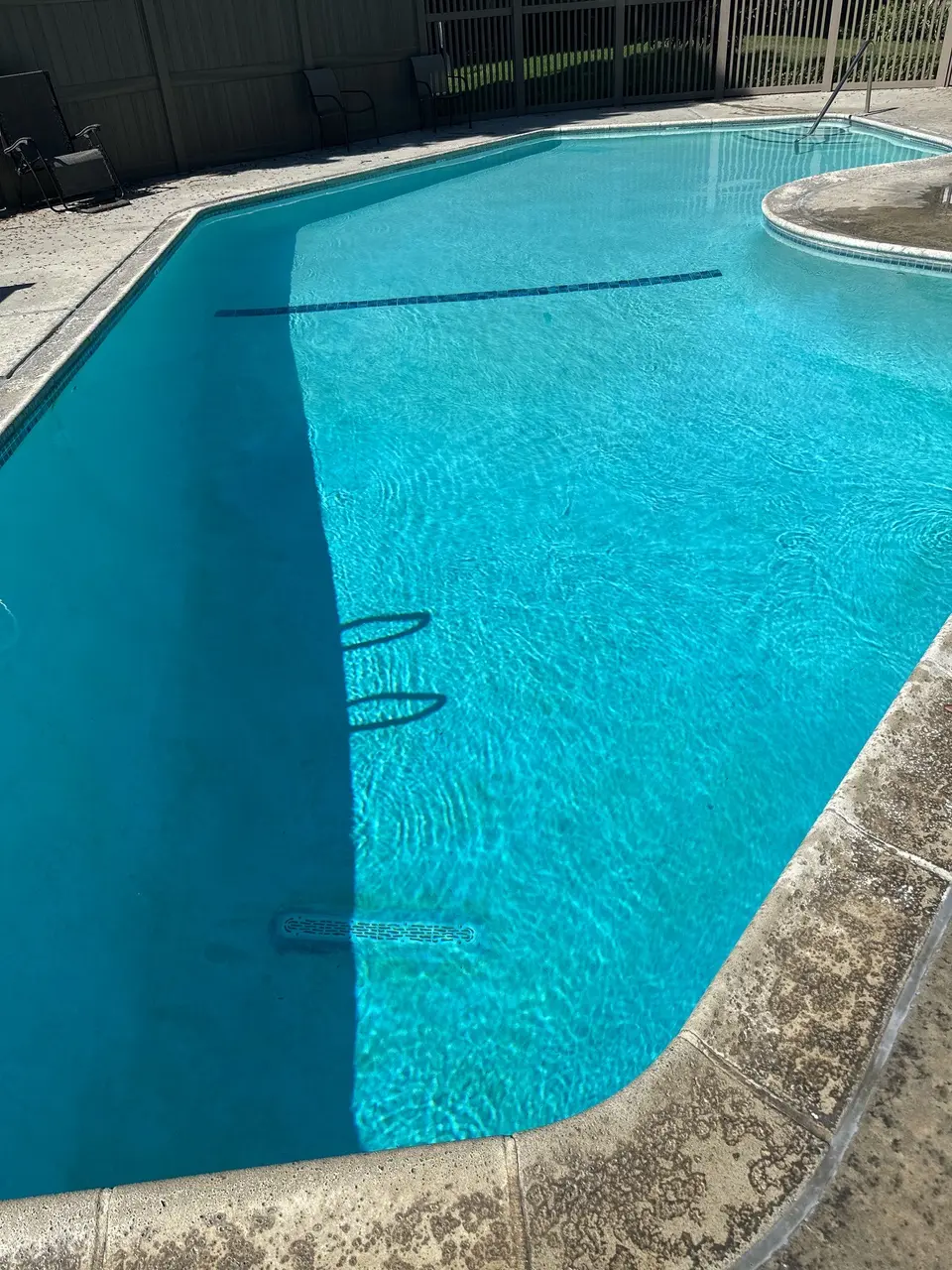 Sparkling turquoise water fills a curved pool with a light finish, underwater tile stripe, and metal handrail, after pool service in Torrance, CA