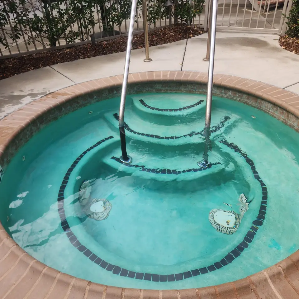 Clear turquoise spa water reveals curved tiled steps and submerged benches beneath stainless steel handrails, after pool service in Torrance, CA