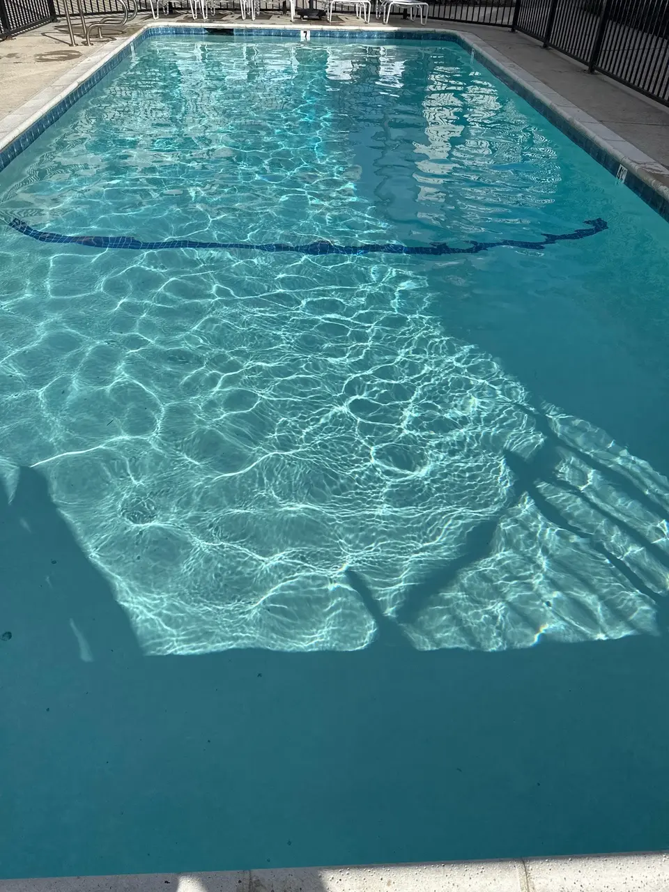 Rectangular pool with sparkling turquoise water, blue tile accents, metal handrails, and poolside seating behind perimeter fencing, after pool service in Torrance, CA