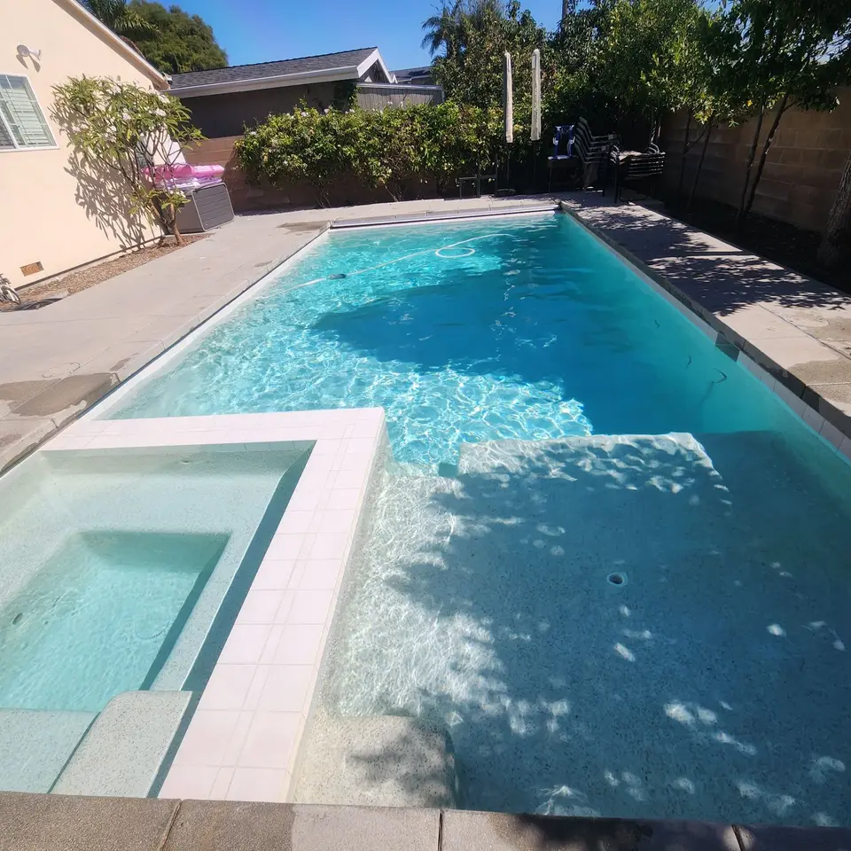 Sparkling turquoise pool and attached spa feature a light finish, wide steps, and surrounding trees and shrubs, after pool service in Torrance, CA