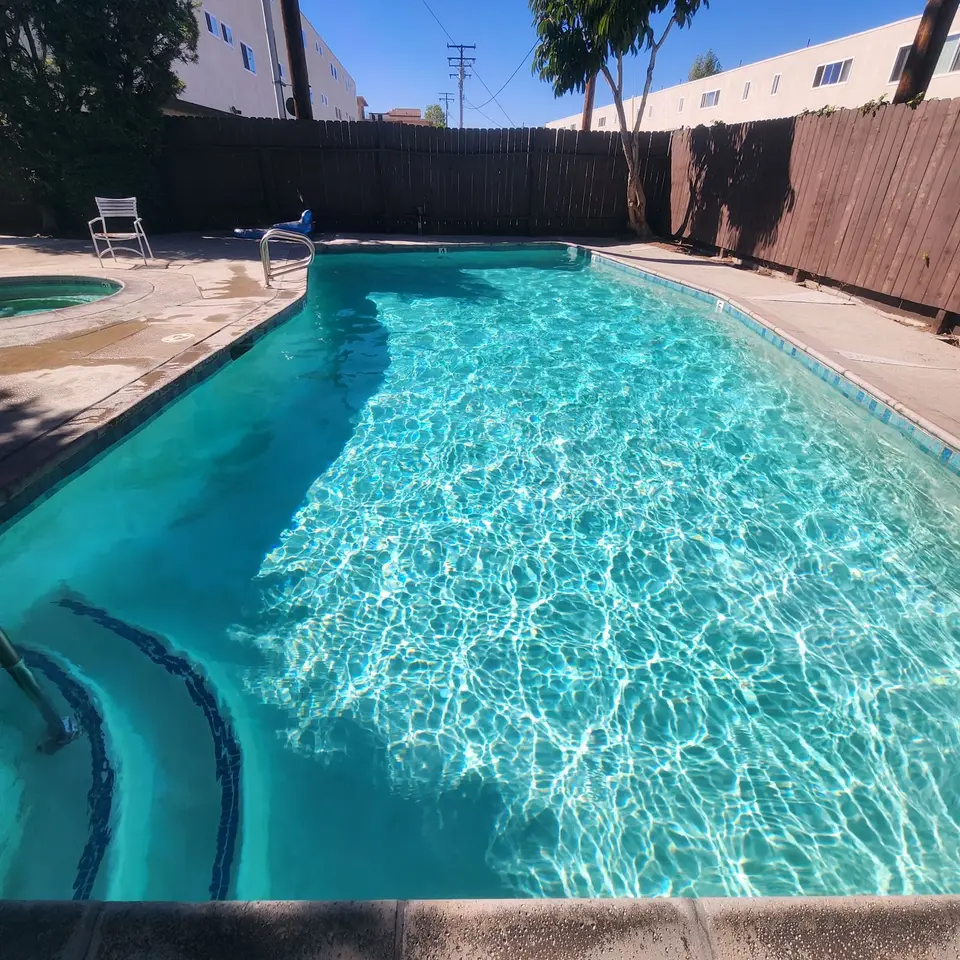 Sparkling turquoise pool with curved entry steps, blue tile, metal handrails, and a separate round spa, after pool service in Torrance, CA
