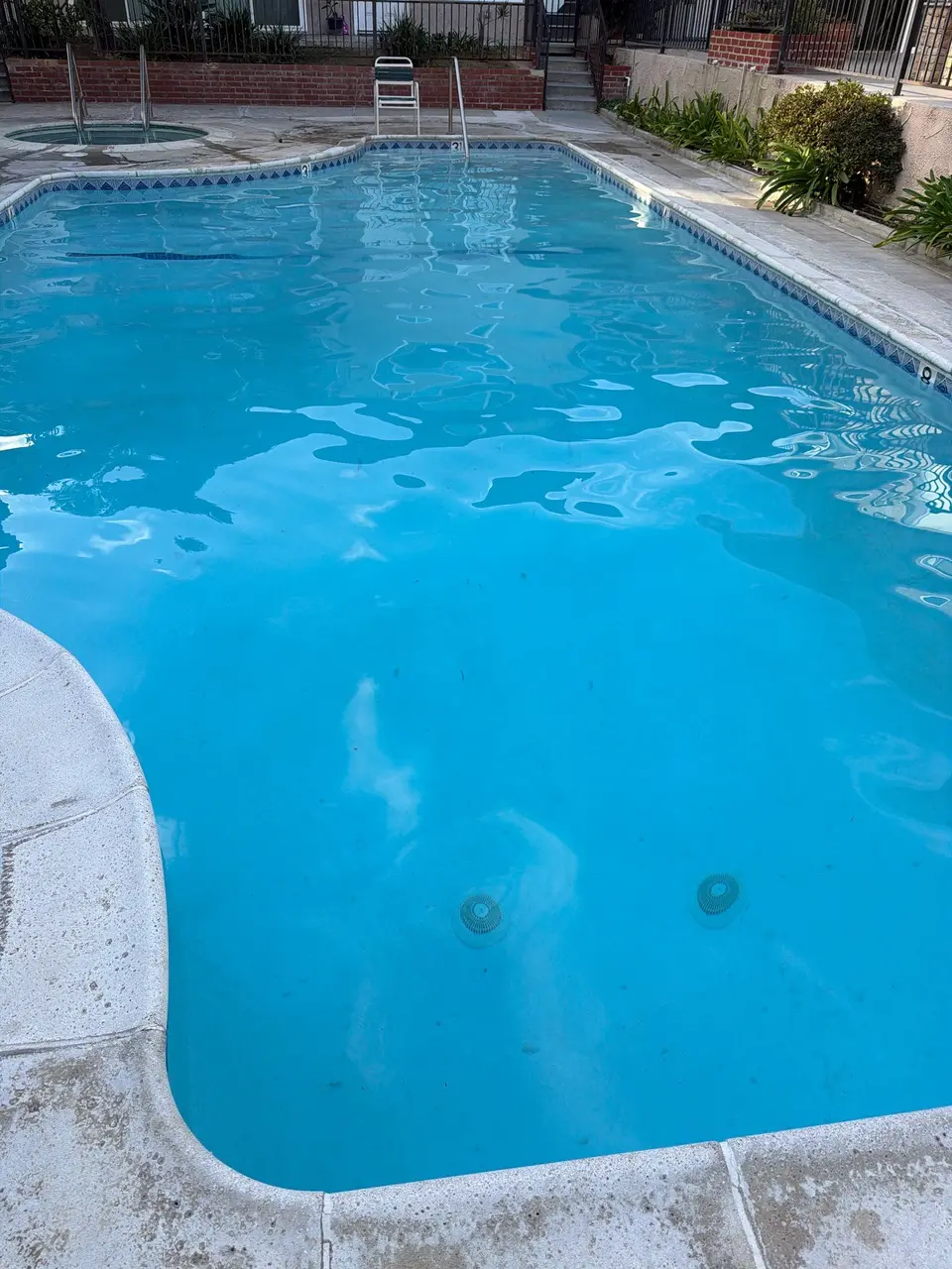 Clear blue pool water with patterned waterline tile, metal ladders, and a round spa beside the deck, after pool service in Torrance, CA