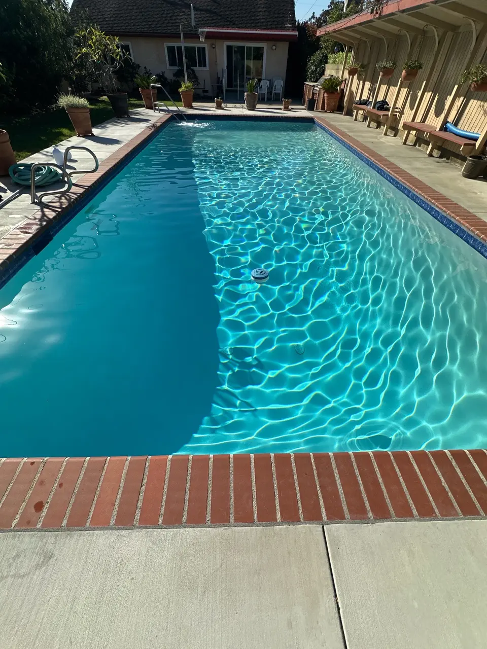Sparkling turquoise water fills a rectangular pool with brick coping, blue tile, metal handrails, and surrounding potted plants, after pool service in Torrance, CA
