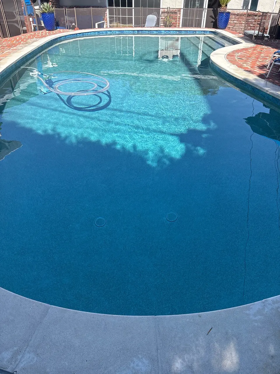 Clear blue pool water reveals the floor and steps, bordered by blue tile, curved coping, and brick decking, after pool service in Torrance, CA