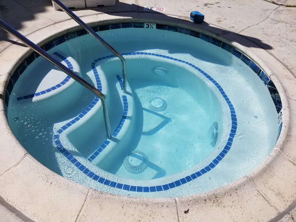 Clear turquoise water fills a circular spa with blue tile trim, curved steps, stainless steel handrails, and bench seating, after pool service in Torrance, CA