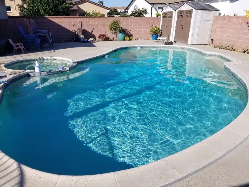 Sparkling blue water fills a curved pool with an attached round spa, decorative tile, and surrounding concrete deck, after pool service in Torrance, CA