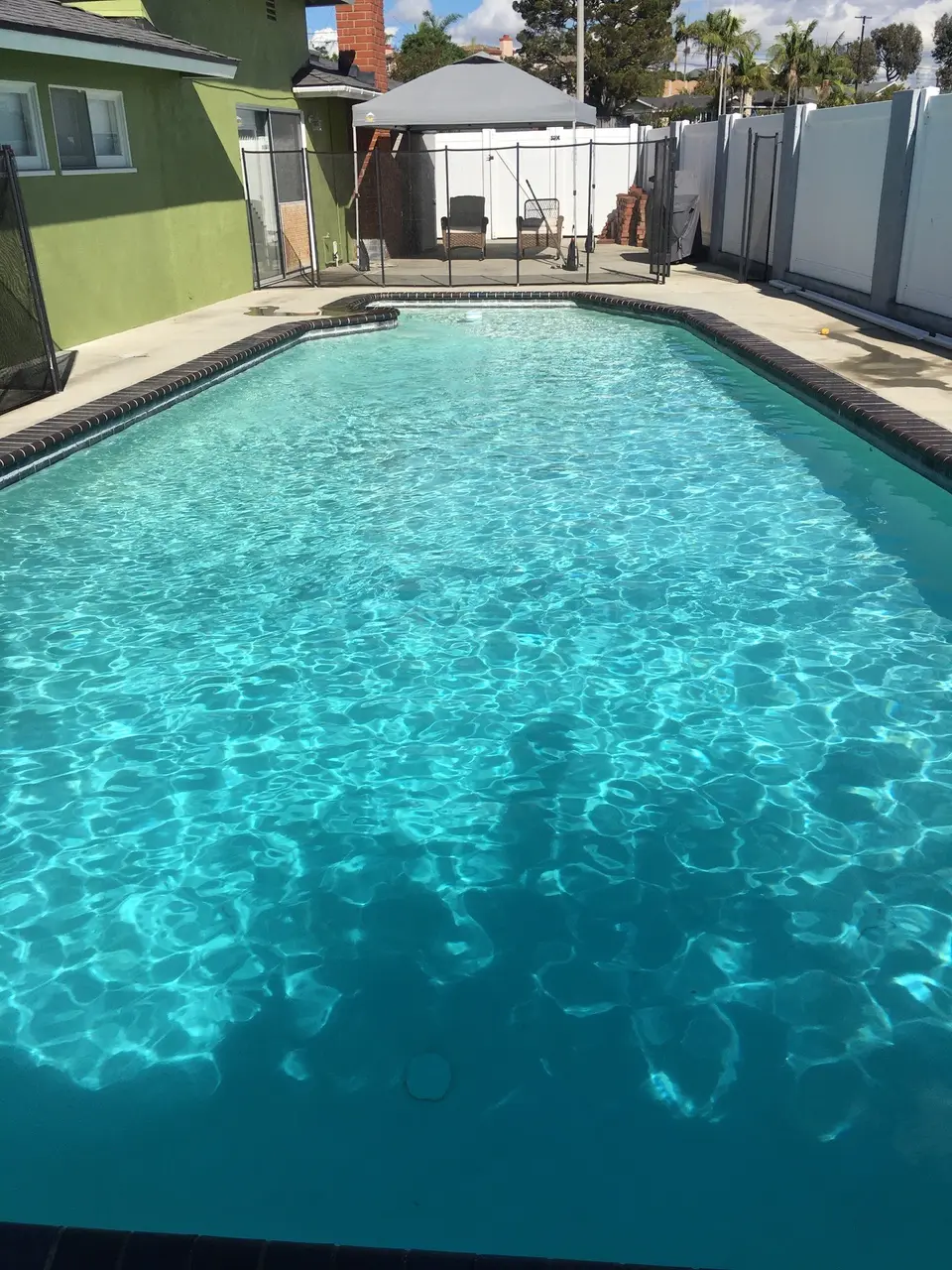 Sparkling turquoise pool water with dark brick coping, safety fencing, and a gazebo beyond the deck, after pool service in Torrance, CA