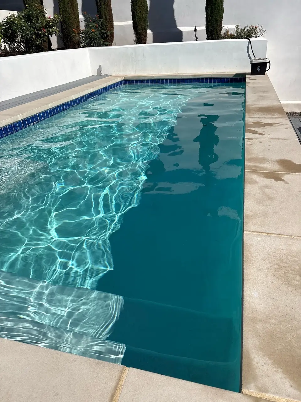 Clear turquoise water fills a rectangular pool with submerged steps, blue waterline tile, and surrounding raised landscaping, after pool service in Torrance, CA