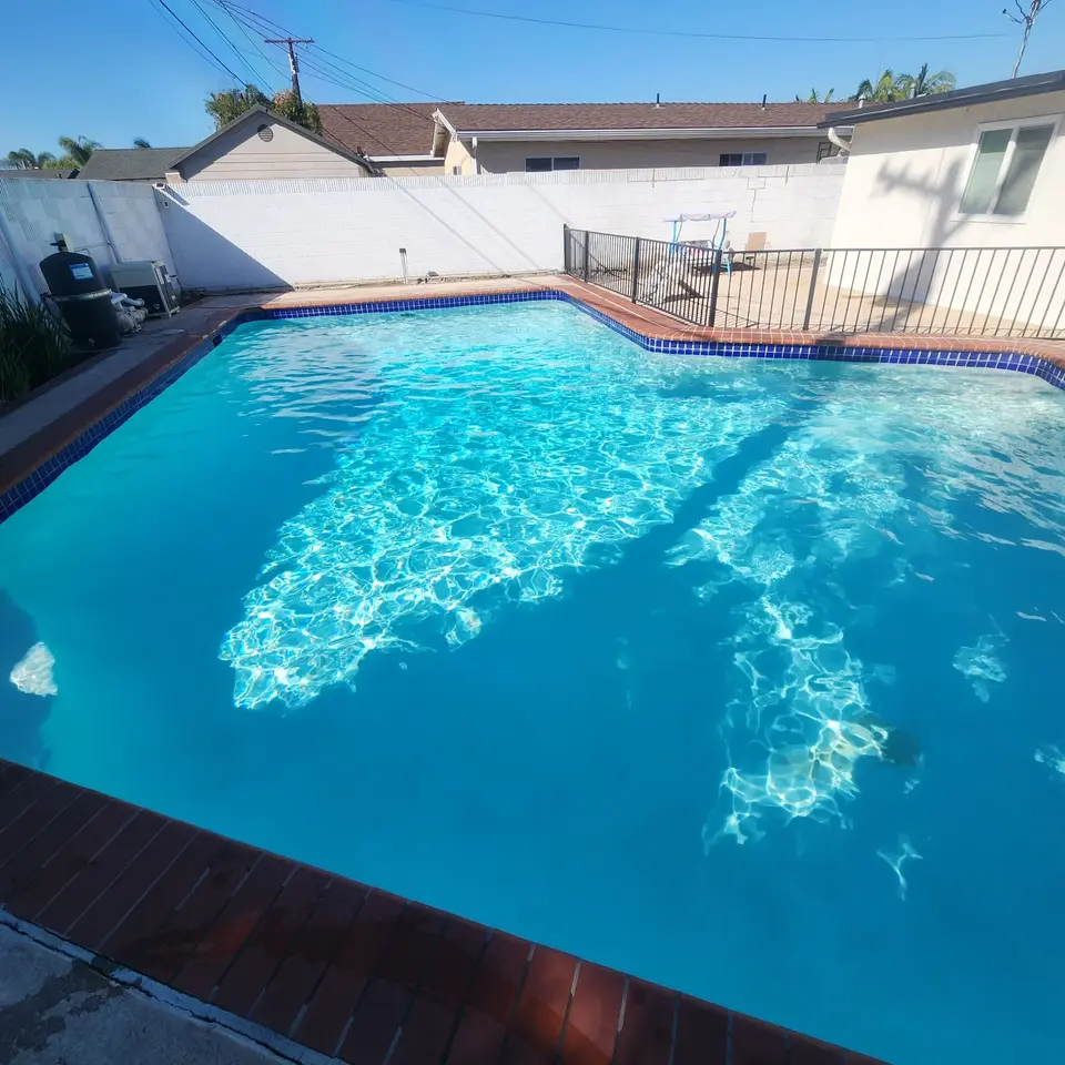 Sparkling turquoise water fills a residential pool bordered by blue tile, brick coping, and a metal safety fence, after pool service in Torrance, CA
