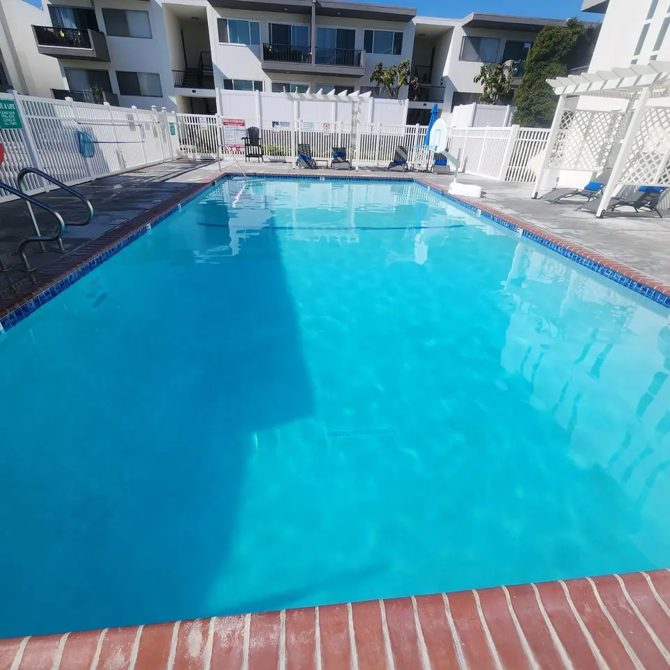 Clear turquoise water fills a rectangular pool with blue tile, brick coping, handrails, and a poolside accessibility lift, after pool service in Torrance, CA